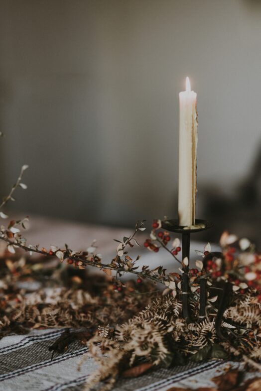 Ett tänt ljus i en ljusstake står på ett bord dekorerat med torkade blommor.